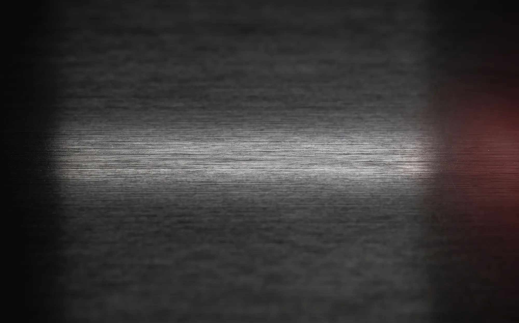 Dark brushed metal crossed by a band of white light, with a red glow at one edge